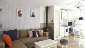 Ein modernes Wohnzimmer mit Sofa, Couchtisch und Kamin. Es gibt eine Küchenzeile mit Geräten und einem Esstisch.
