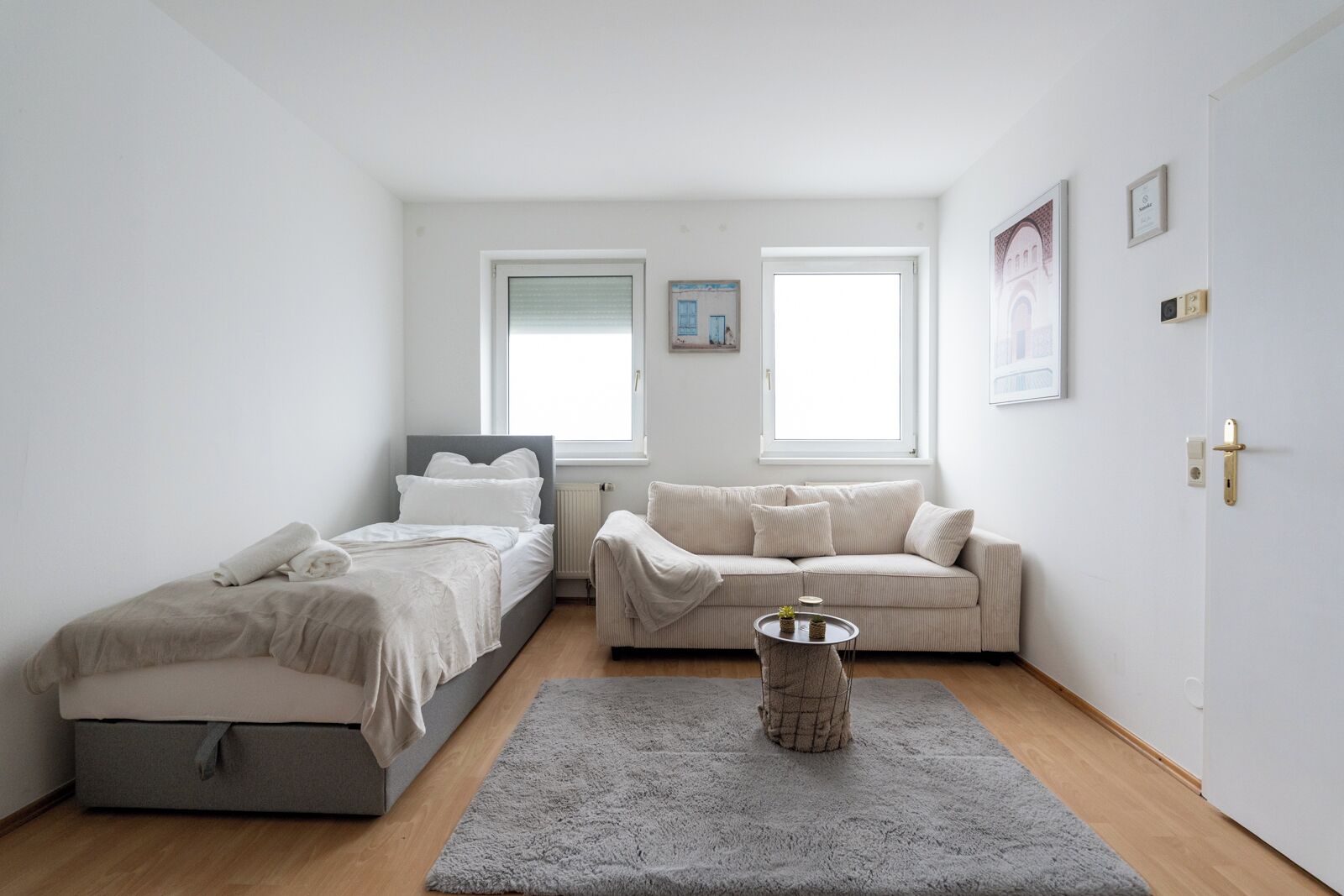 Un dormitorio con cama, sofá, una mesita y ventana.