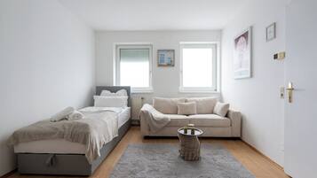 Un dormitorio con cama, sofá, una mesita y ventana.
