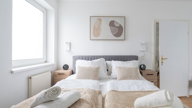 Une chambre à coucher avec un grand lit, deux tables de chevet, un radiateur, une fenêtre et une porte.