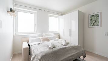 Un dormitorio moderno con cama, dos ventanas, un radiador, un armario y una obra de arte floral enmarcada en la pared.