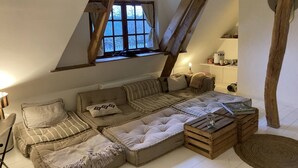 A cozy loft bedroom with a large sectional sofa, a wooden coffee table, and a window with a view of trees. - La LongeMer: Countryside & Sea Just a few kilometers from Veules-Les-Roses (Angiens)