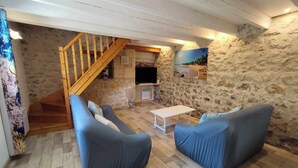 A cozy living room with a stone wall, wooden staircase, and a flat-screen TV. - Le Marais Salant - Gites for 8 people with swimming pool at Logis de Chalons à la mer (Le Gua)