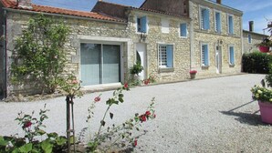 A stone building with a gravel driveway, a window with a shutter, and potted plants. - Le Marais Salant - Gites for 8 people with swimming pool at Logis de Chalons à la mer (Le Gua)
