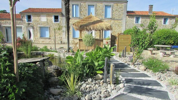 A stone building with a thatched roof structure, surrounded by a garden with a stone pathway. - Le Marais Salant - Gites for 8 people with swimming pool at Logis de Chalons à la mer (Le Gua)