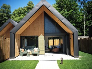 A modern house with a sloped roof, wooden exterior, and a large glass door leading to a living area with a sofa and a dining table. - Domaine Le Verbois (Saint-Maximin)