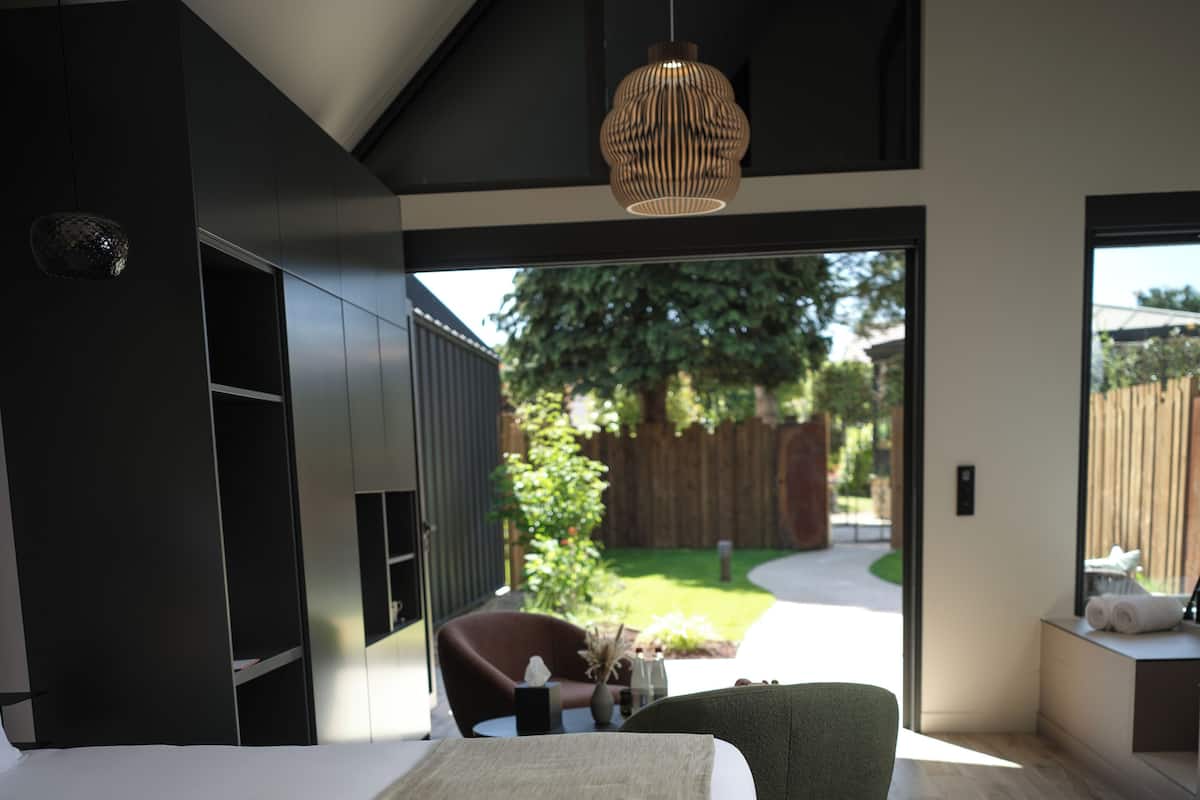 A modern bedroom with a large bed, a seating area with a chair and table, and a view of the outdoors.