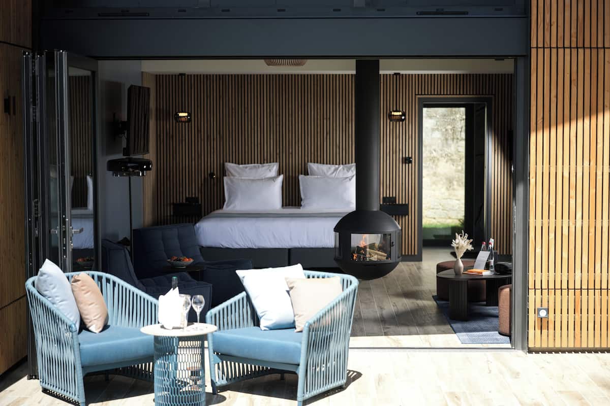 A modern bedroom with a large bed, a hanging fireplace, and a balcony with seating.