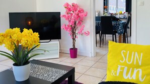 A living room with a TV, a table with yellow flowers, a pink flower arrangement, and a 'SUN & Fun' pillow. - Spacious townhouse - 2 self-contained apartments for flexible living (Quimperlé)