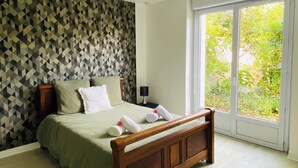A bedroom with a geometric-patterned wall, a wooden bed frame, and a large window with a view of greenery. - Spacious townhouse - 2 self-contained apartments for flexible living (Quimperlé)