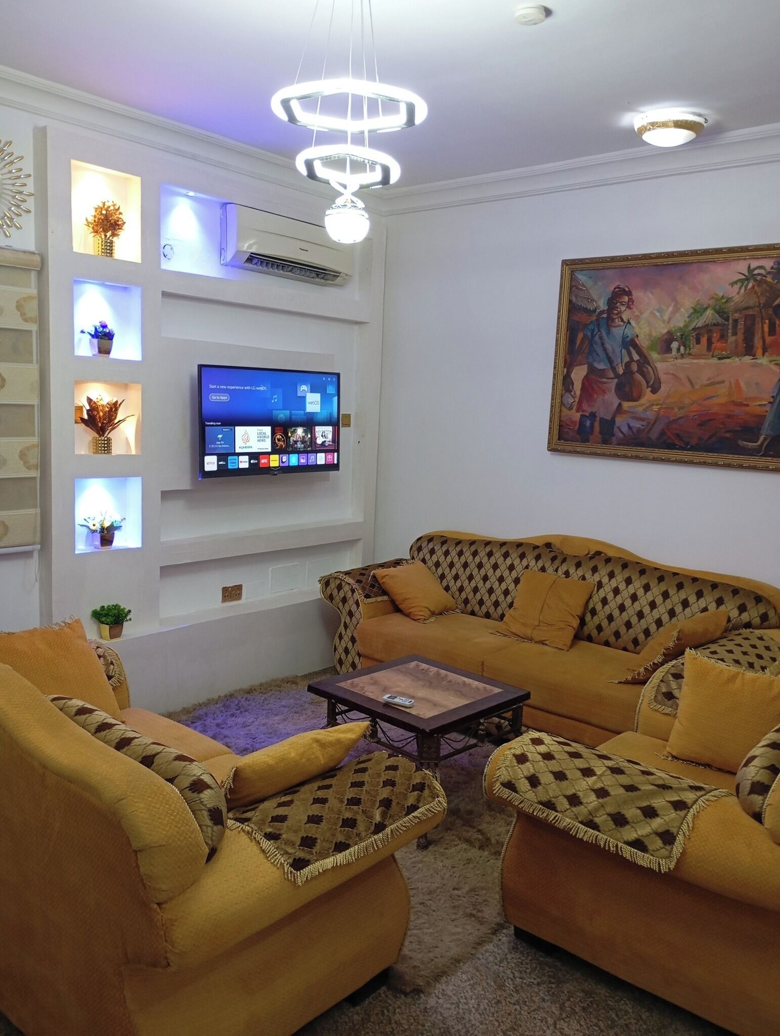 A living room with a sofa set, a coffee table, a flat-screen TV mounted on the wall, and a painting on the wall.
