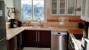 A kitchen with a dishwasher, a coffee maker, and a window with a view of trees. - Mas Picton, 4 bedroom house with swimming pool, 10 min from the beach (Argelès-sur-Mer)