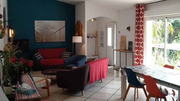 A living room with a red sofa, blue armchair, and a dining area with a table and chairs. - Mas Picton, 4 bedroom house with swimming pool, 10 min from the beach (Argelès-sur-Mer)