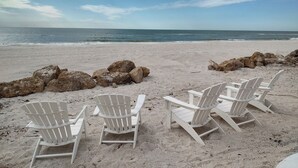 Une plage avec des chaises longues blanches et de gros rochers.