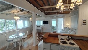Une cuisine compacte équipée d’une cuisinière, d’un coin repas avec des chaises et d’un téléviseur fixé au mur.