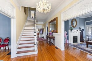 Eine prächtige Treppe führt zu einer Empore mit einem Chandelier, einem Kamin und einem großen Spiegel.