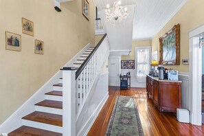 Eine Treppe mit weißen Geländern und Holzstufen führt zu einem Raum mit einem Chandelier, einem Holzschrank und einem Teppich.