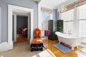 Ein Badezimmer mit einer freistehenden Badewanne, einem Sessel und einem dekorativen Raumteiler.