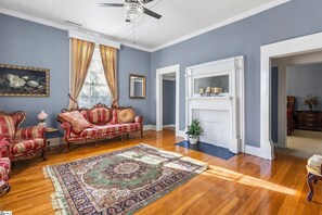 Ein Zimmer mit Kamin, einer roten und goldenen Sofagarnitur, einem großen Teppich mit Muster und einem Deckenventilator.