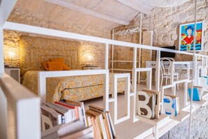 Ein gemütliches Schlafzimmer mit einer Steinwand, einem Bett mit floralem Bettzeug und einem Bücherregal voller Bücher.
