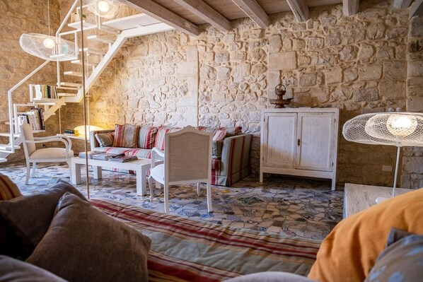 Una habitación acogedora con pared de piedra, escalera blanca, sofá, armario y suelo estampado.