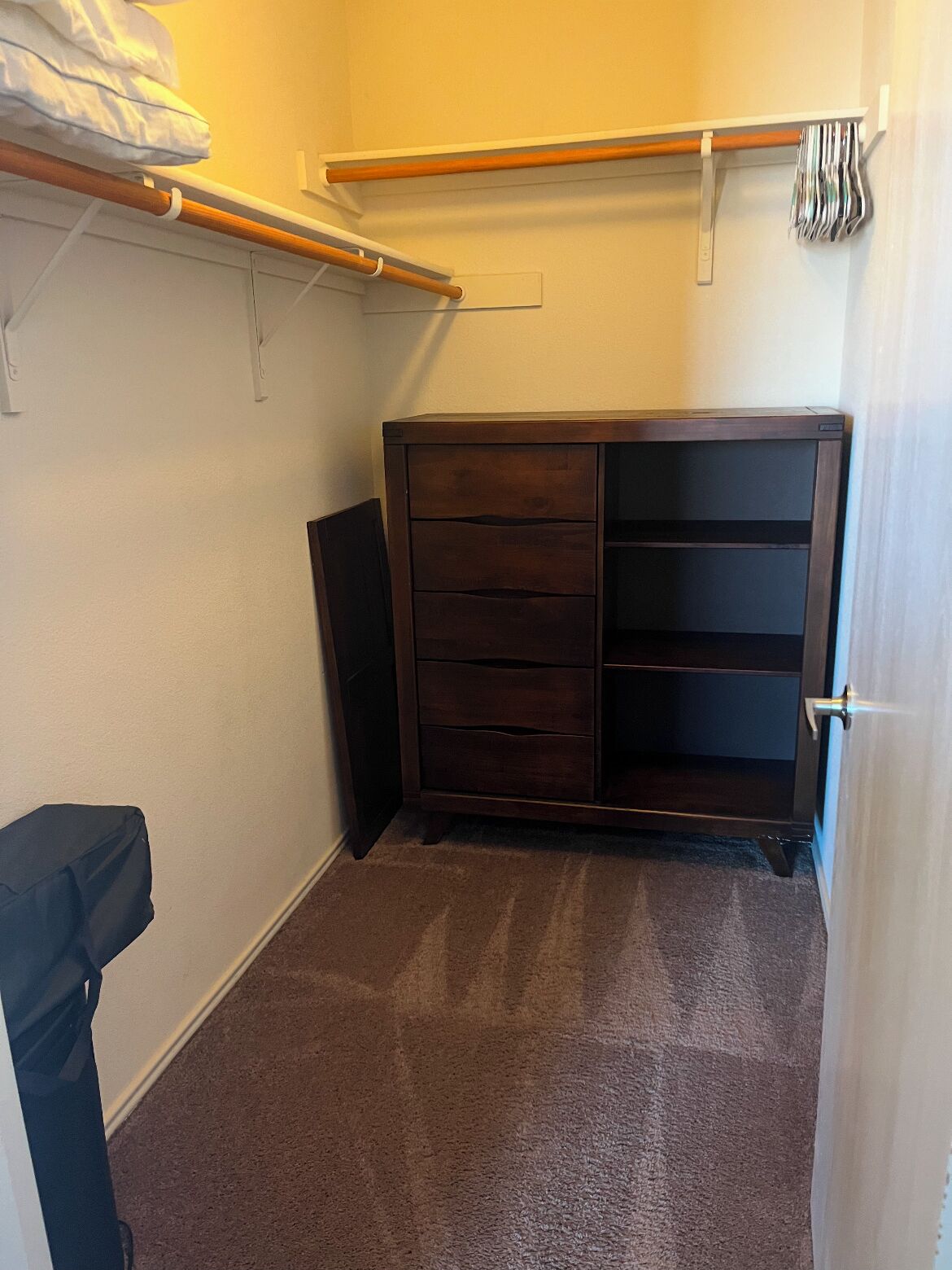 A small, carpeted closet with a wooden dresser and a hanging rod.