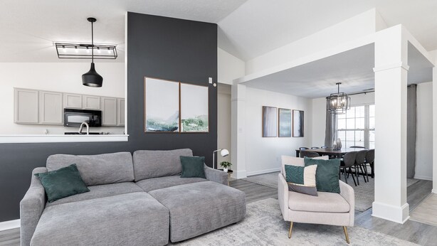 Una sala moderna con un sofá seccional gris, un sillón pequeño y una zona de comedor al fondo.