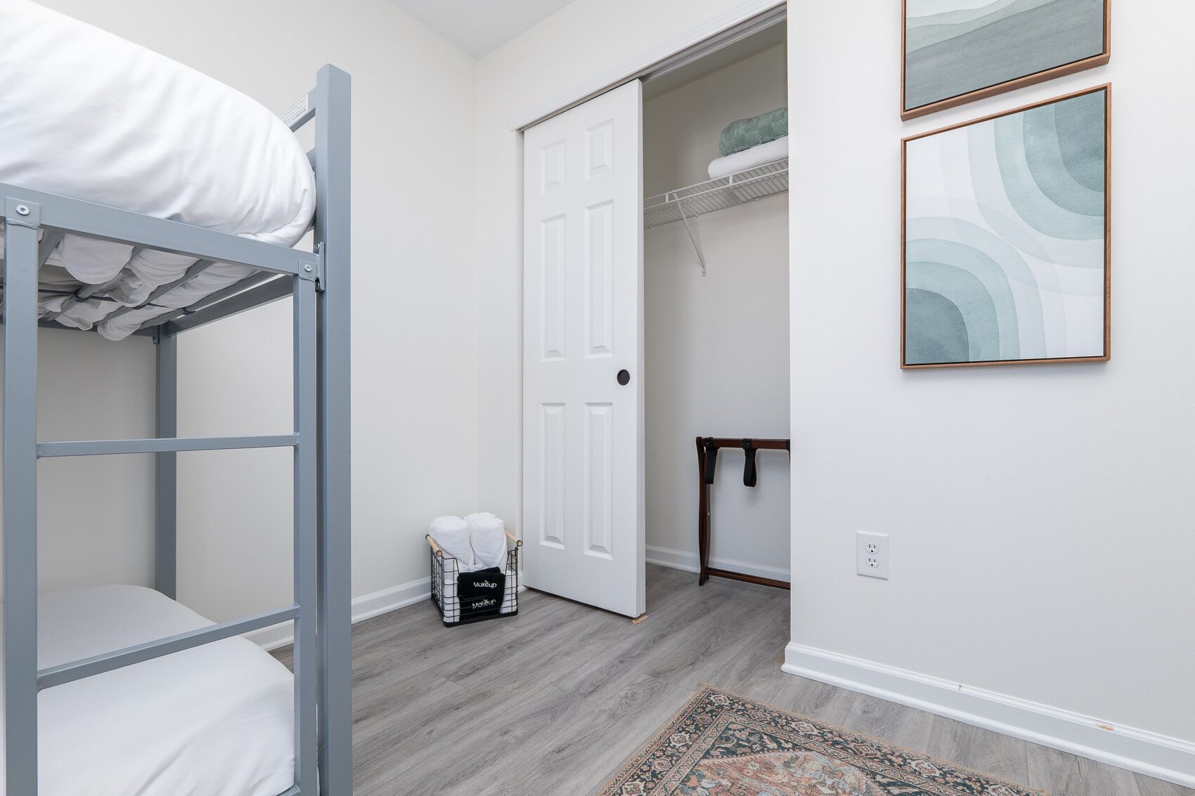 A bedroom with a bunk bed, a wardrobe, a small table, and a door leading to another room.