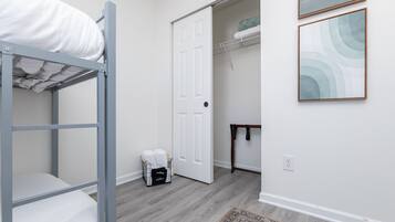 A bedroom with a bunk bed, a wardrobe, a small table, and a door leading to another room.
