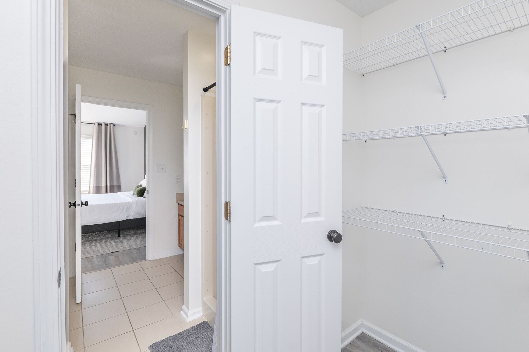 A room with a bed, a bathroom with a shower, and a white door.