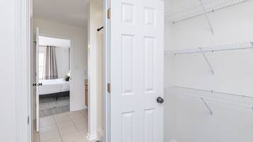 A room with a bed, a bathroom with a shower, and a white door.