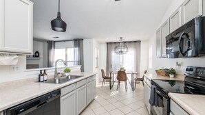 Una cocina moderna con lavavajillas, estufa y microondas. Hay una zona de comedor con mesa y sillas.