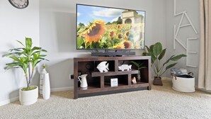Una sala de estar con un televisor de pantalla plana sobre un soporte de madera, rodeada de plantas y adornos.