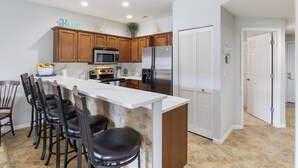 Una cocina moderna con armarios de madera, un refrigerador de acero inoxidable, un microondas y una barra con taburetes.