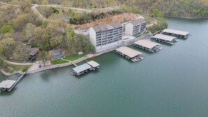 Un hotel de varios pisos con un muelle y barcos, rodeado de colinas boscosas.