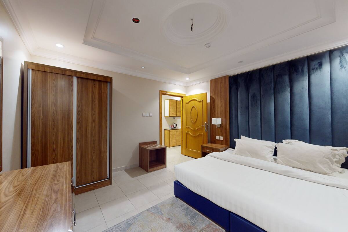 A modern bedroom with a large bed, wooden wardrobe, and a built-in wardrobe with a mirror.