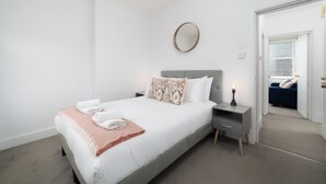 A modern bedroom with a neatly made bed, a bedside table with a lamp, and a mirror on the wall. - 
Stylish Apartment Close to Fulham Palace (London)