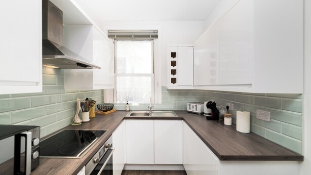 A modern kitchen with white cabinets, a dark countertop, a built-in stove, and a window above the sink. - 
Stylish Apartment Close to Fulham Palace (London)