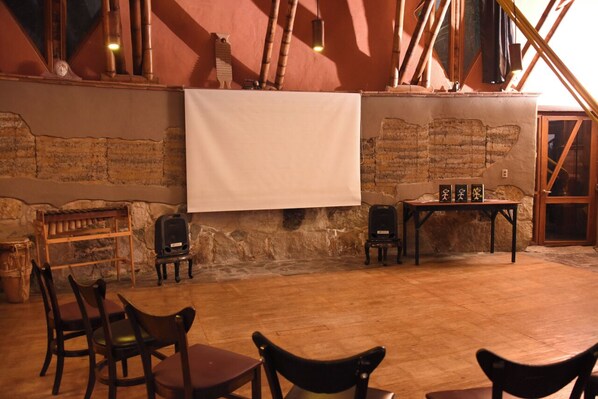 A rustic interior with exposed brick walls, wooden furniture, and a large blank projection screen. - Reserva Botánica Choachí (Choachí)