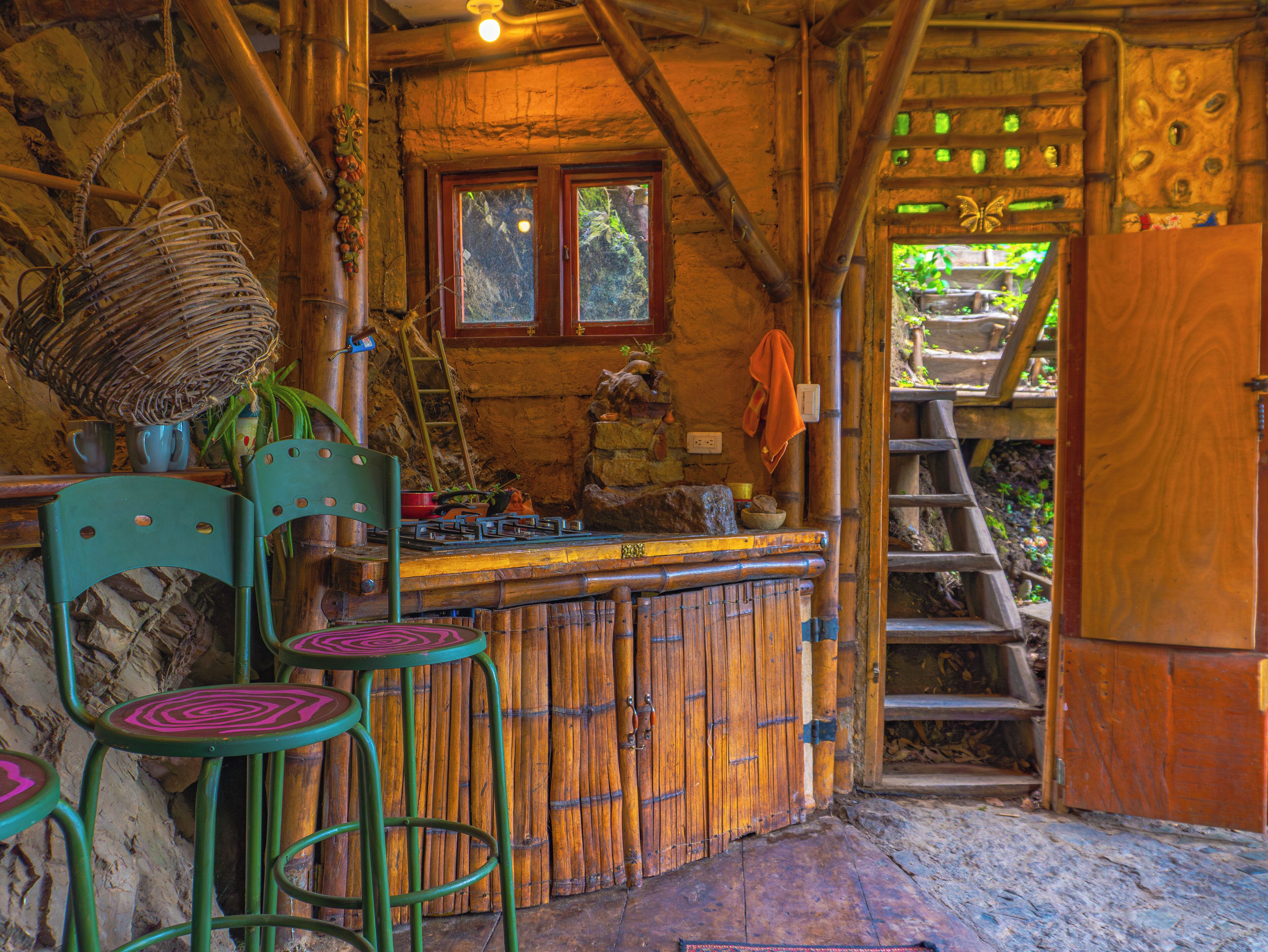 A rustic wooden interior with a bar area, stools, and a ladder leading to an outdoor area.