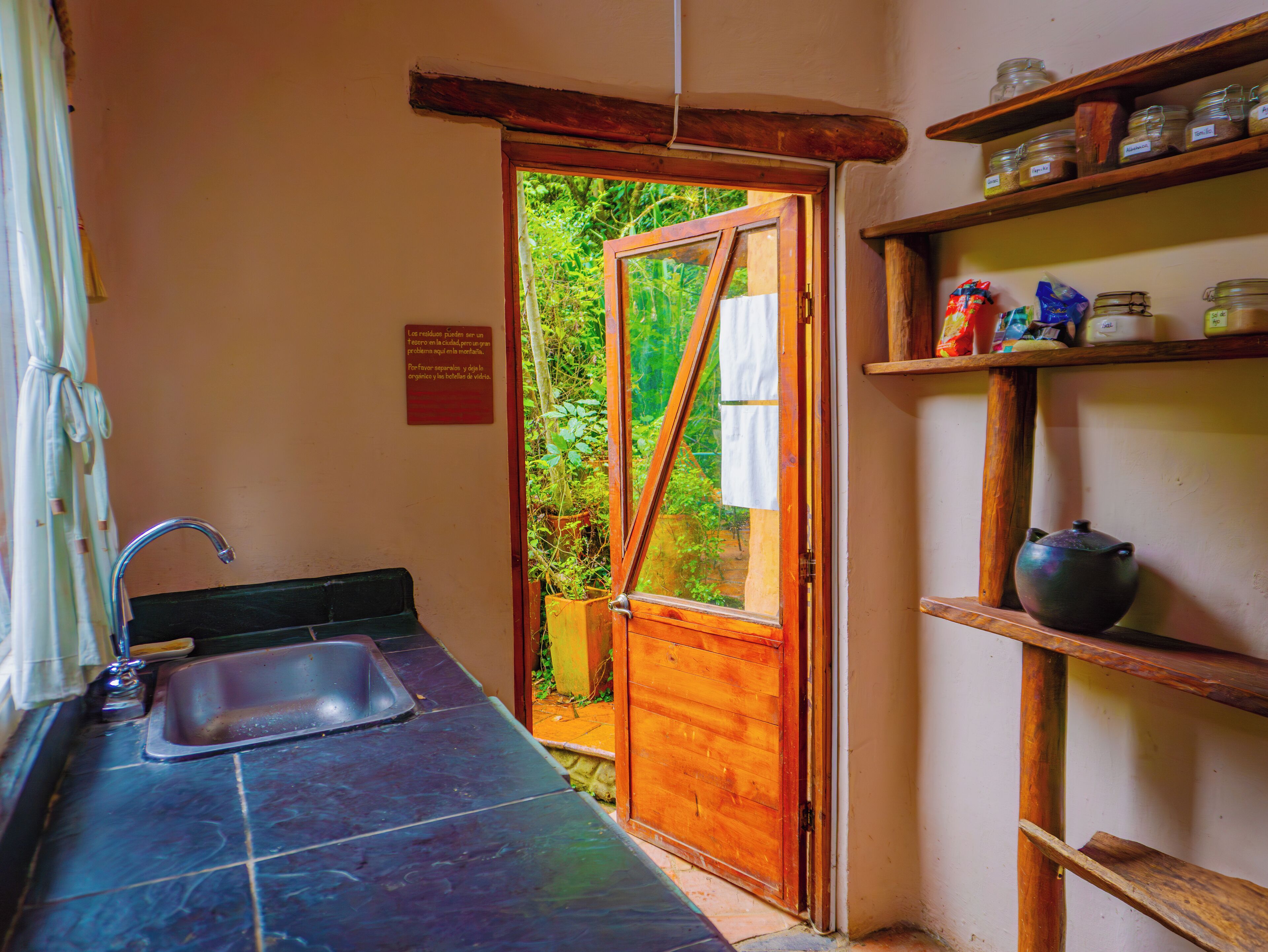 A kitchen with a sink, wooden door, and shelves with jars.
