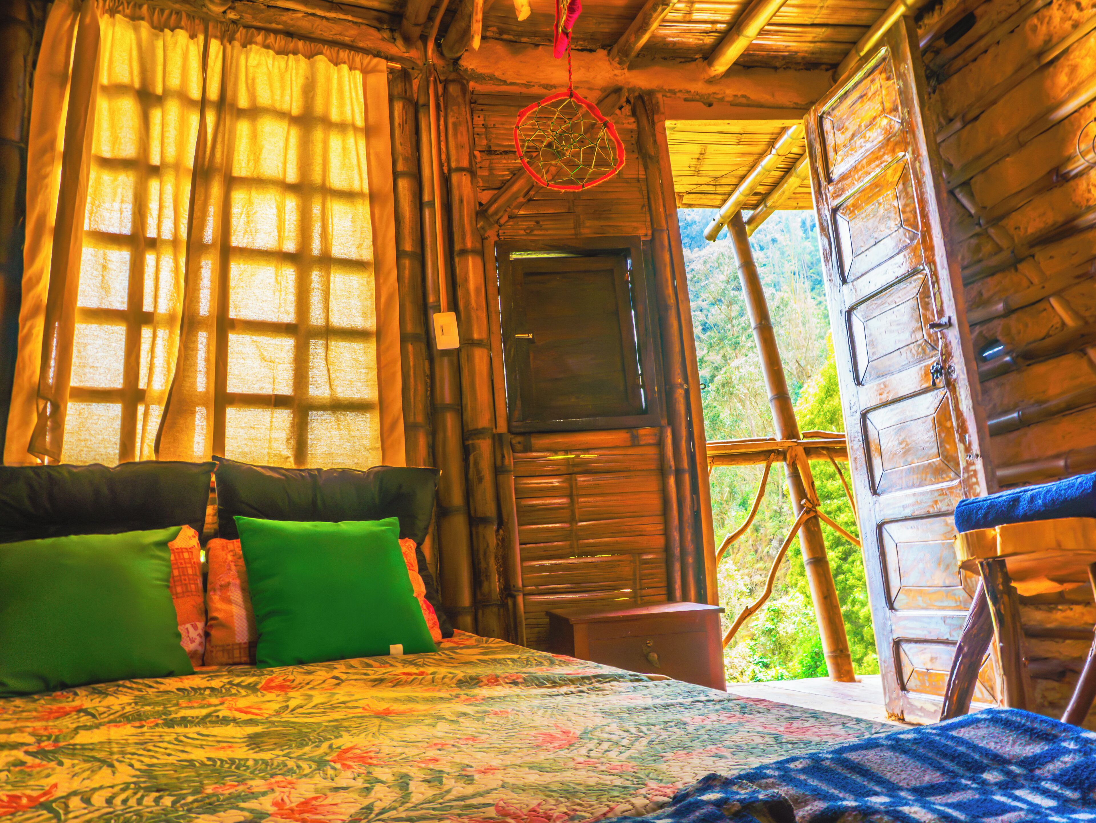 Una habitación rústica de madera con una cama, almohadas verdes, un atrapasueños y vistas al exterior.