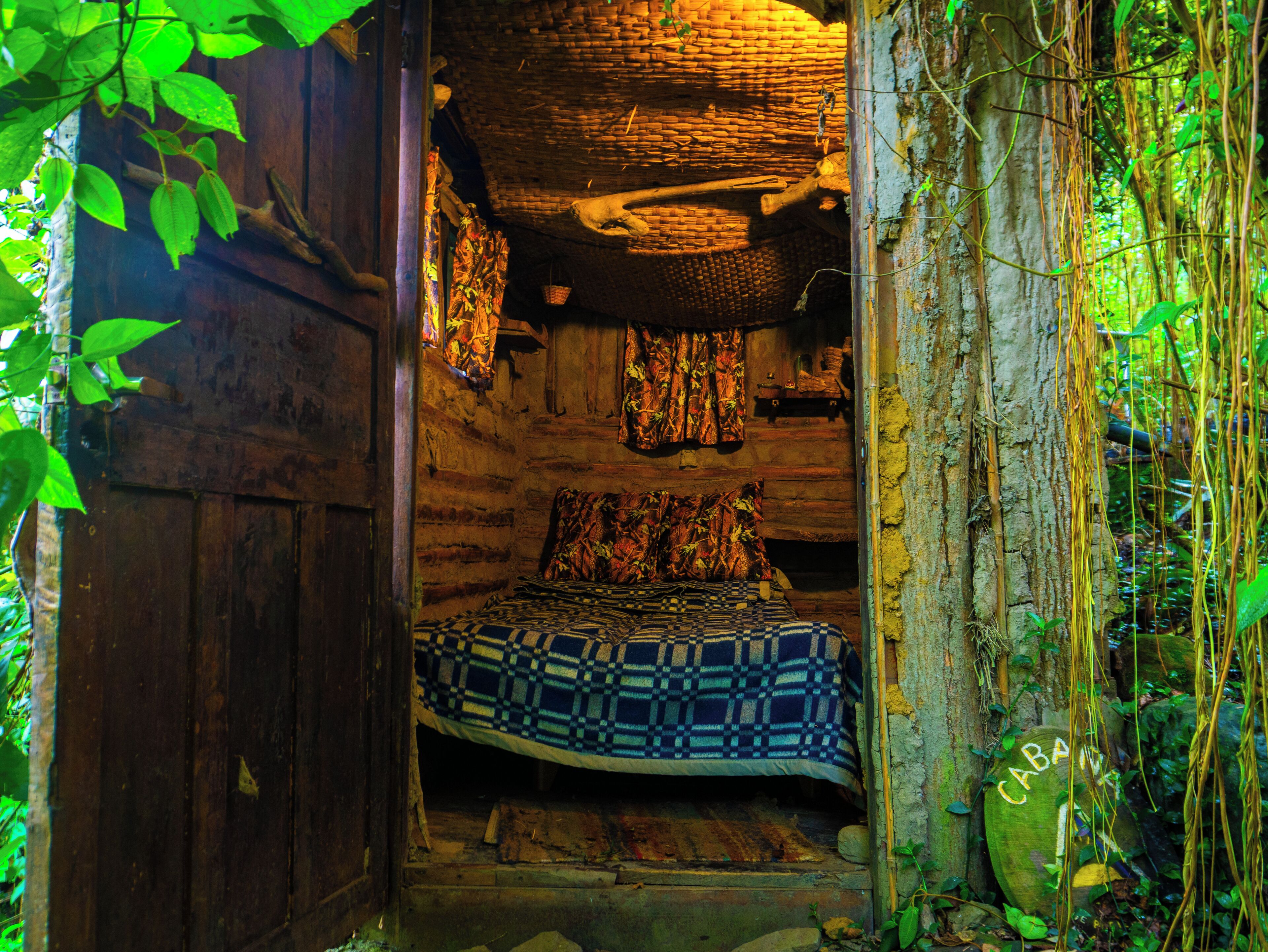 A rustic wooden cabin with a bed, a woven ceiling, and a natural surrounding.