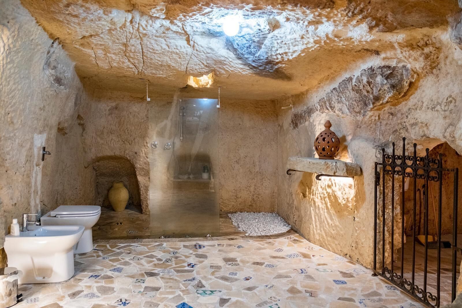 Une salle de bain rustique avec un sol en pierre, des toilettes blanches, un bidet et un espace douche.