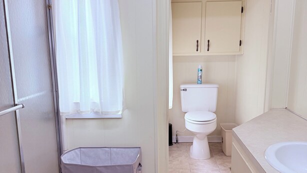 Un bagno con un water, un lavandino, una doccia e un cestino.