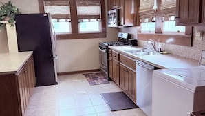 A kitchen with wooden cabinets, a black refrigerator, a stove, and a white washing machine. - Downtown Convenience near Lake Norman (Mooresville)