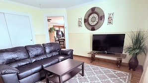 A living room with a black leather sofa, a coffee table, a TV, and a ceiling fan. - Downtown Convenience near Lake Norman (Mooresville)