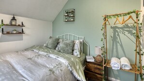 A bedroom with a bed, bedside table, lamp, and a wall-mounted shelf with plants. - Cozy Trafford Cottage Just 14 Minutes from Airport (Partington)