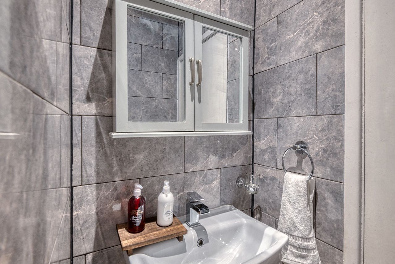 Ein Badezimmer mit weißem Waschbecken, einer Holzwaschtischplatte, einer Duschkabine aus Glas und einer Wand mit Marmorfliesen.