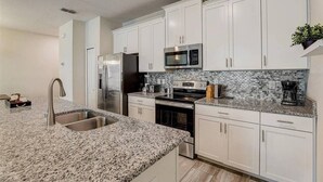A modern kitchen with white cabinets, granite countertops, stainless steel appliances, and a tiled backsplash.